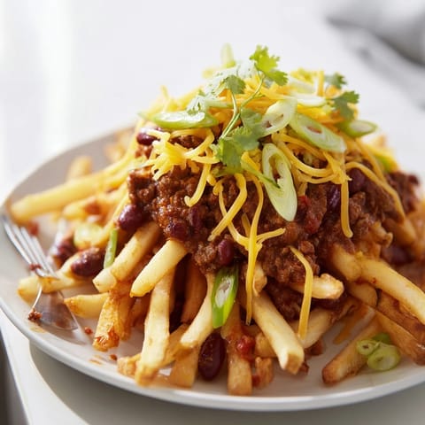 Chili Cheese Fries loaded with hearty chili, sharp cheddar, and fresh scallions on a platter.