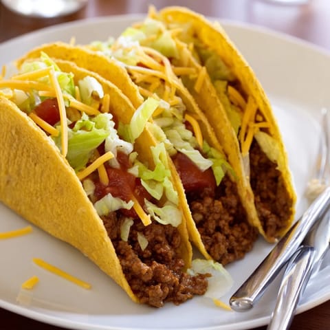 Golden crunchy taco shells filled with seasoned beef, fresh veggies, and lime wedges on the side.