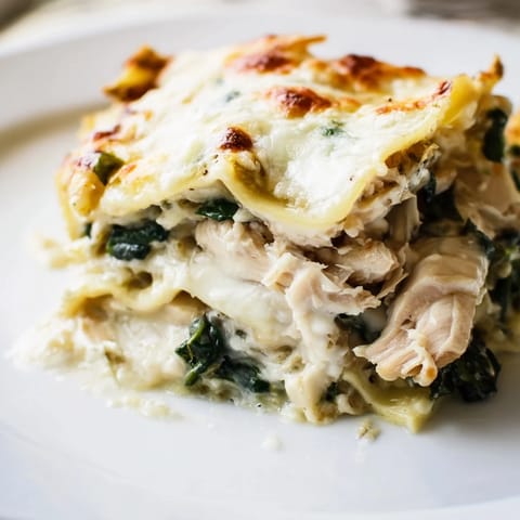 A close-up slice of Chicken Alfredo Lasagna reveals tender pasta sheets and rich, velvety Alfredo sauce between hearty layers.
