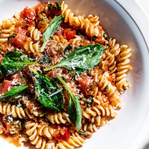 Tomato spinach one-pot rotini served hot from the stove, garnished with freshly grated Parmesan cheese alongside a slice of crusty bread.  