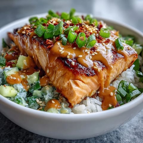 Tender salmon fillet topped with spicy bang bang sauce in a rice bowl with lime wedges and fresh cilantro garnish. 