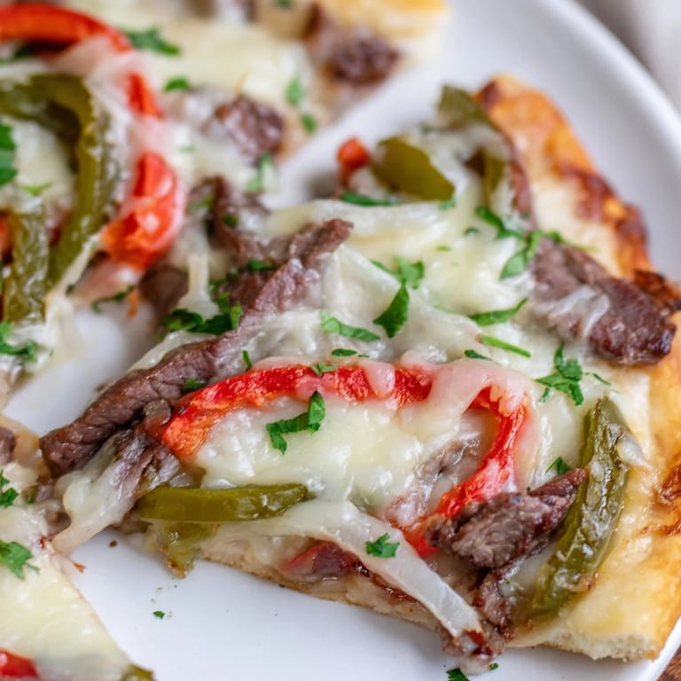 Freshly baked crust holds savory ribeye, sautéed onions, and peppers on this appetizing Philly Cheesesteak Pizza.