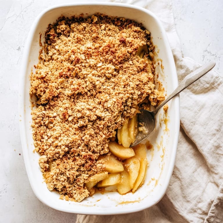 A close-up of bubbling Apple Crumble, featuring spiced apple slices peeking through a crispy, buttery crumble in a rustic baking dish.