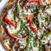 Golden, bubbly provolone and mozzarella melt over a loaded Philly Cheesesteak Pizza, with tender steak and vibrant peppers peeking through.