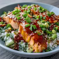 Flaky baked salmon rests on jasmine rice beside a vibrant cucumber-edamame salsa, all drizzled with creamy bang bang sauce. 