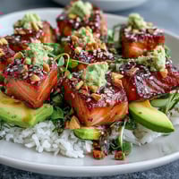 Golden-brown seared salmon cubes rest on fluffy sushi rice, topped with creamy sliced avocado, crisp cucumber, and fresh spring onions in a vibrant bowl.